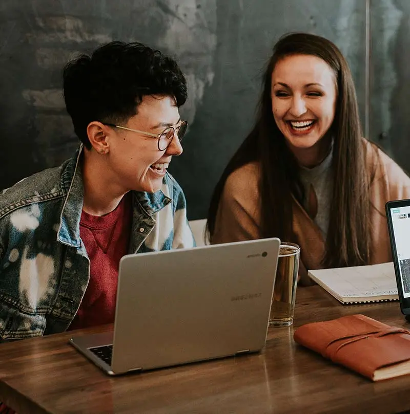 Smiling couple sitting at a table with a laptop and drinks, enjoying a light-hearted moment